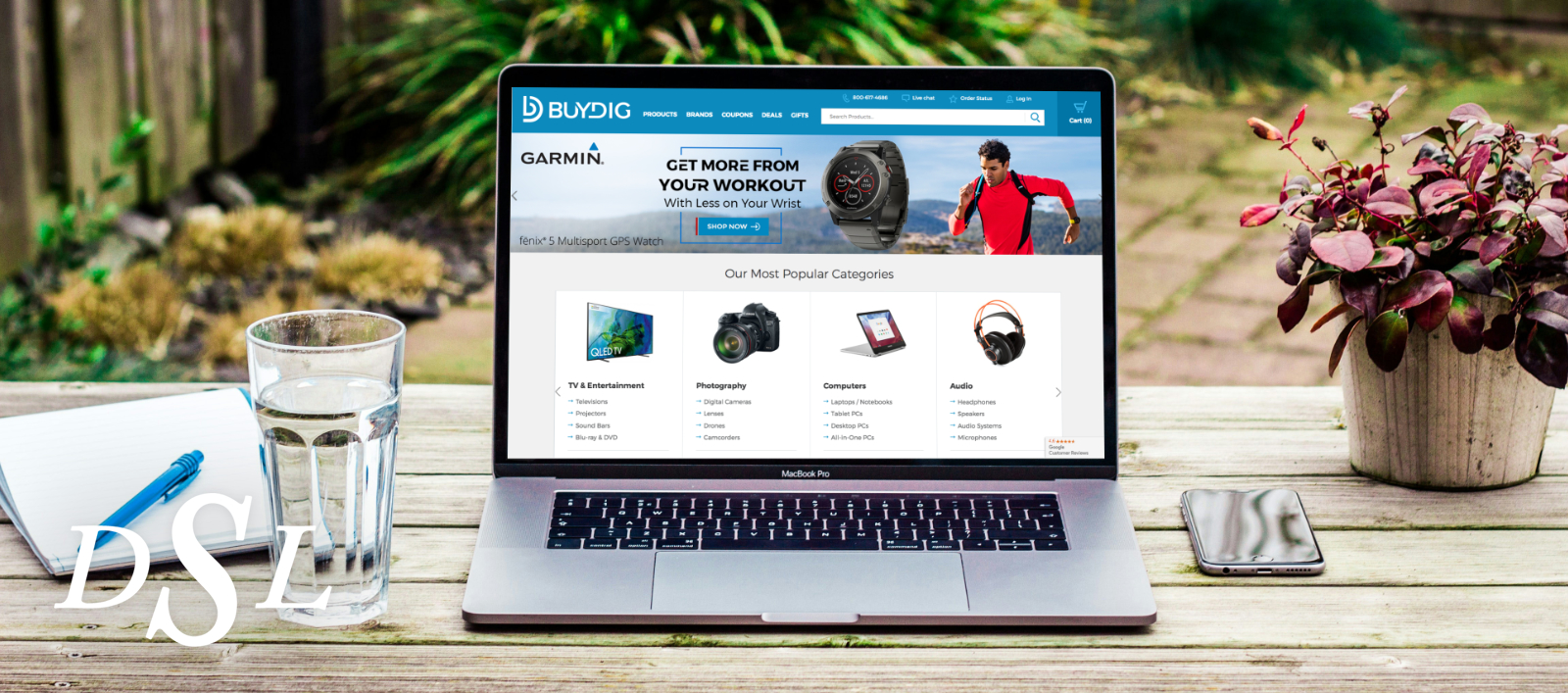 A laptop displaying the Buydig.com home page and Garmin Fenix 5 GPS watch banner.