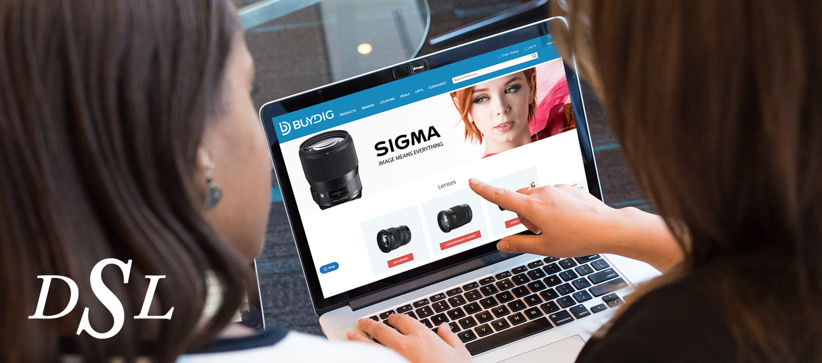 Two women looking and pointing at a laptop screen displaying Buydig's Sigma landing page.